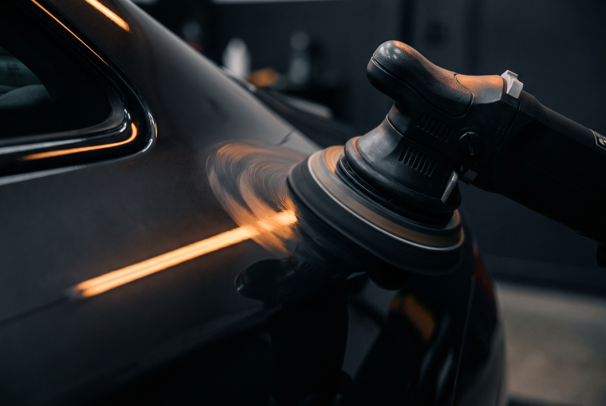 Dual action polisher buffing the black paintwork of a car in a dark detailing bay